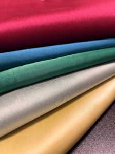 Selymes fényű szatén textilek gazdag színválasztéka egymásra hajtva: magenta, királykék, smaragdzöld, ezüst és arany.